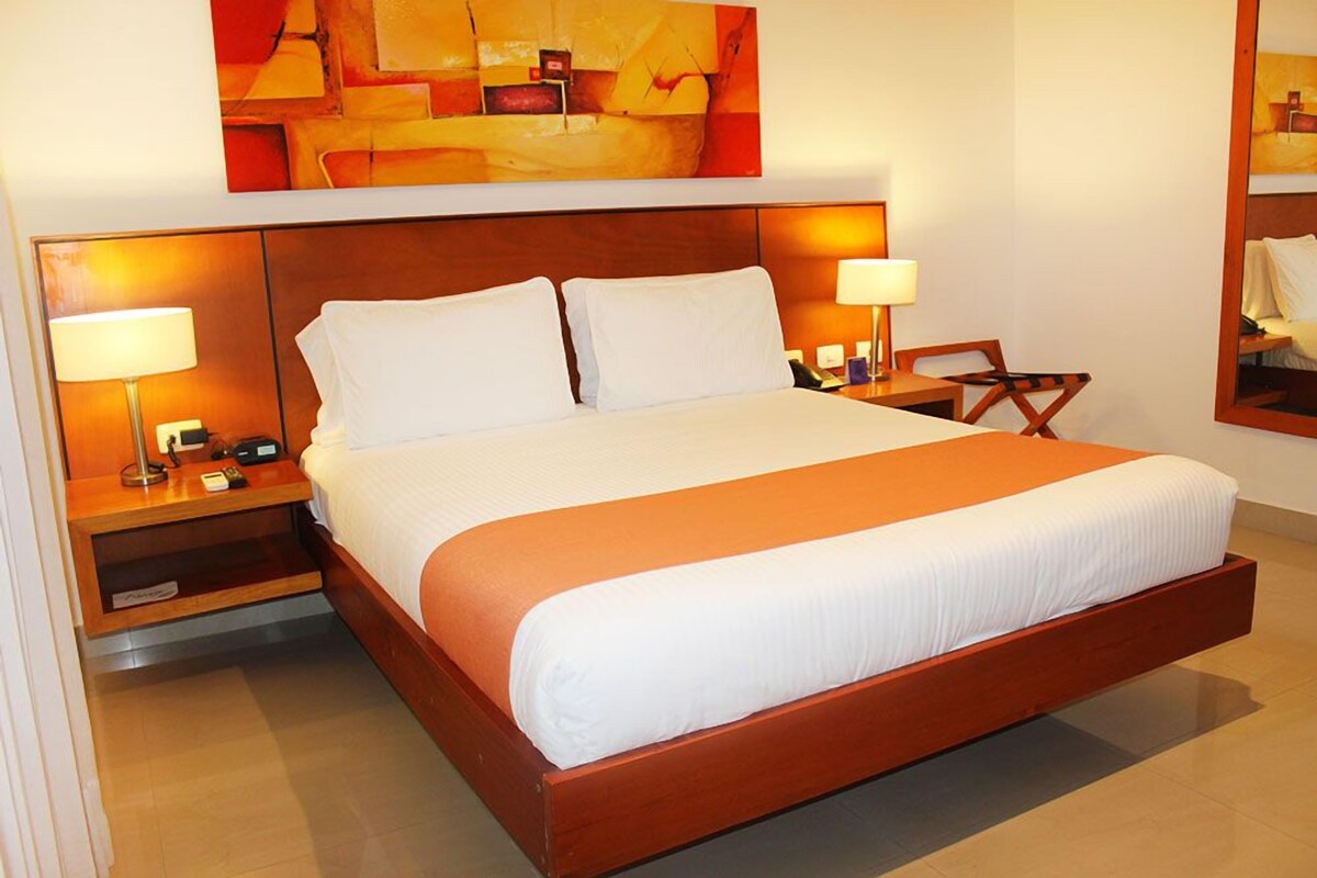 Habitación de hotel con una cama grande, dos mesitas de noche con lámparas, un escritorio y una silla.