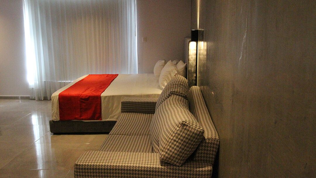 Une chambre d’hôtel avec un lit, un canapé et un luminaire fixé au mur.