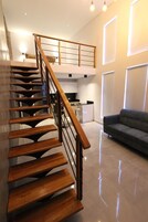 Un interior moderno con una escalera de madera que conduce a un dormitorio en entrepiso, una zona de cocina y una sala de estar con sofá.