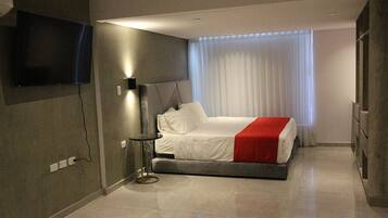 A modern hotel room with a bed, a flat-screen TV mounted on the wall, and a large window with curtains.