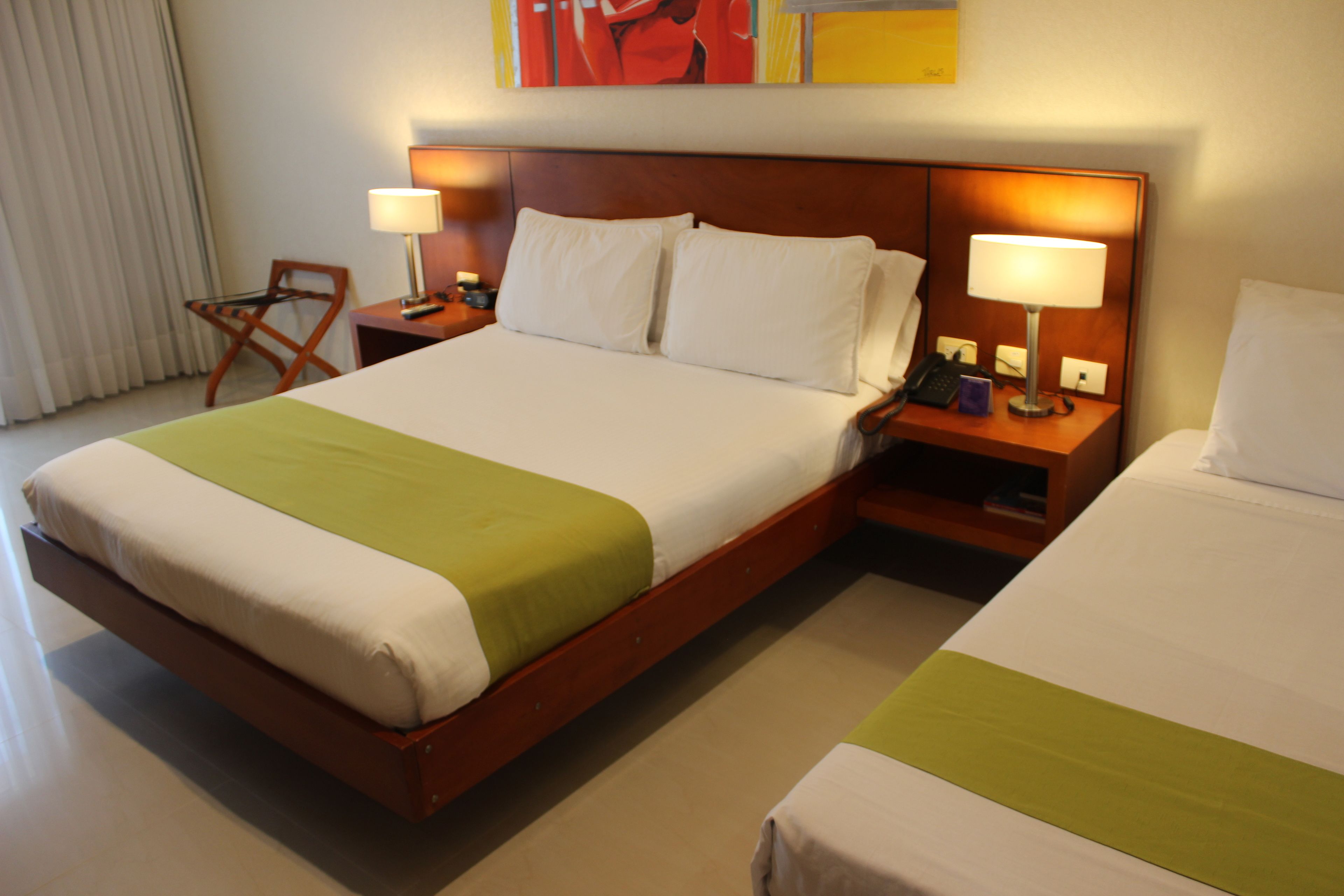 Una habitación de hotel con una cama grande, dos mesitas de noche, una silla y un cuadro en la pared.