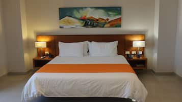 A hotel room with a large bed, two bedside tables with lamps, a painting on the wall, and a bright orange accent on the bedspread.