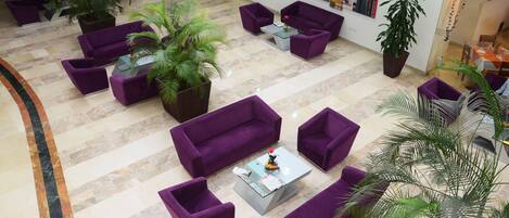 A spacious lobby with purple sofas, a glass coffee table, and multiple potted plants.