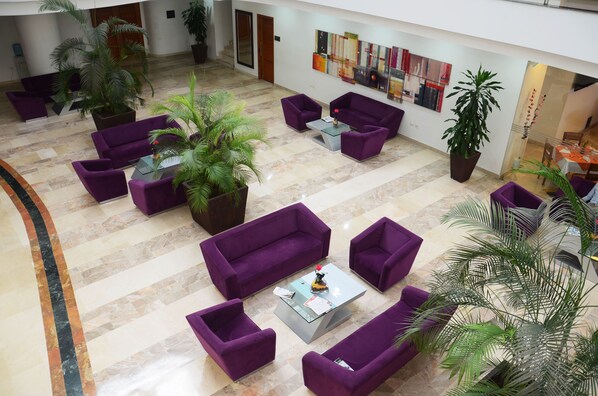 Un vestíbulo amplio con sofás morados, una mesa de centro de vidrio y varias plantas en macetas.