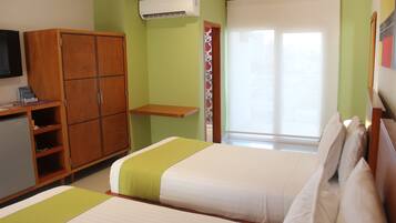 Habitación de hotel con dos camas, un armario, un escritorio con ordenador y una ventana con persianas.