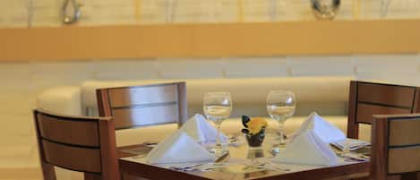 A dining table set with white napkins, silverware, and wine glasses, surrounded by wooden chairs.