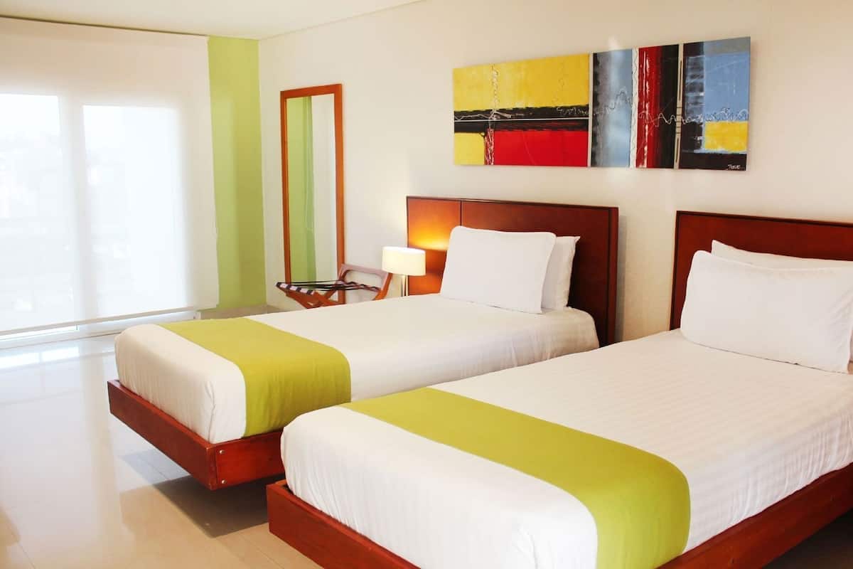 A hotel room with two beds, a mirror, a lamp, and a painting on the wall.