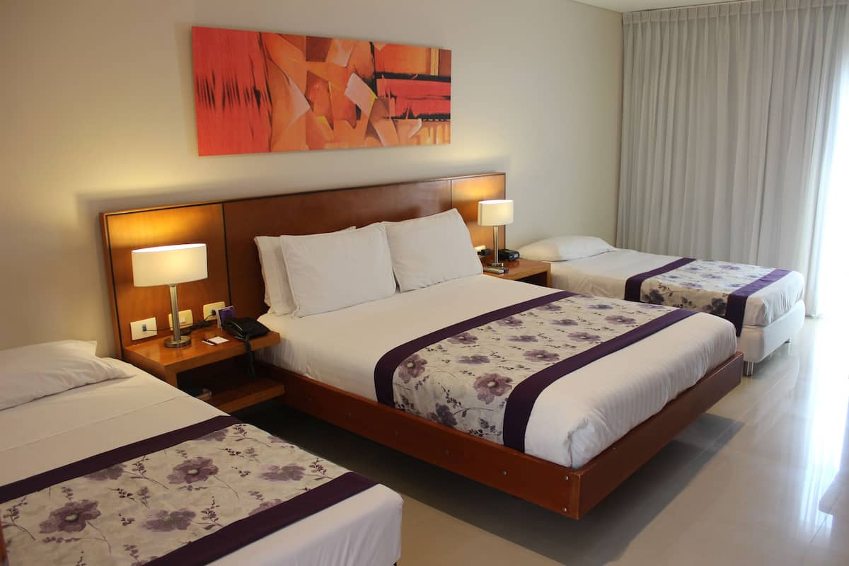 A hotel room with a large bed, two smaller beds, a nightstand with a lamp, and a painting on the wall.