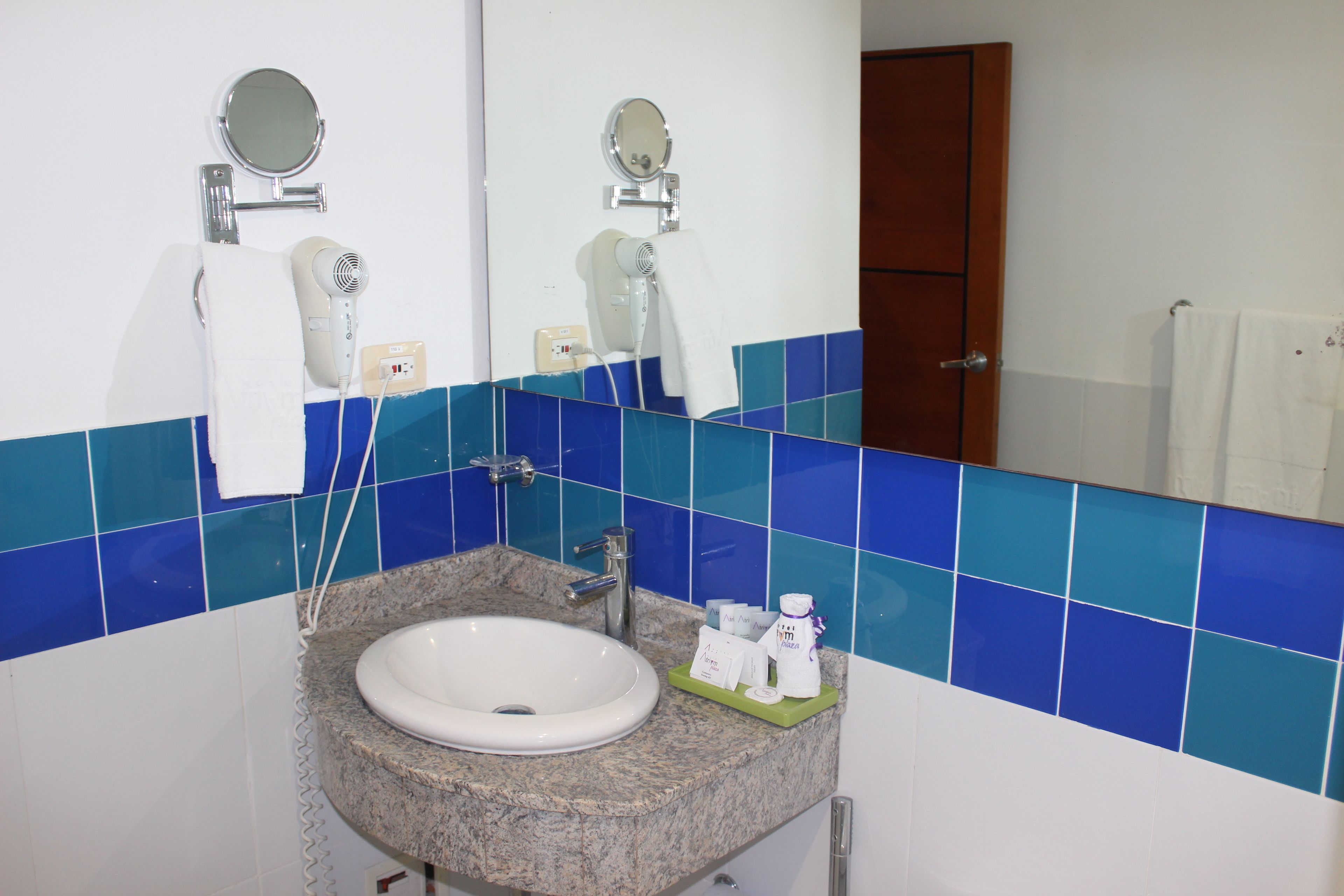 Un bagno con un lavandino bianco, piastrelle blu, uno specchio e un porta asciugamani.