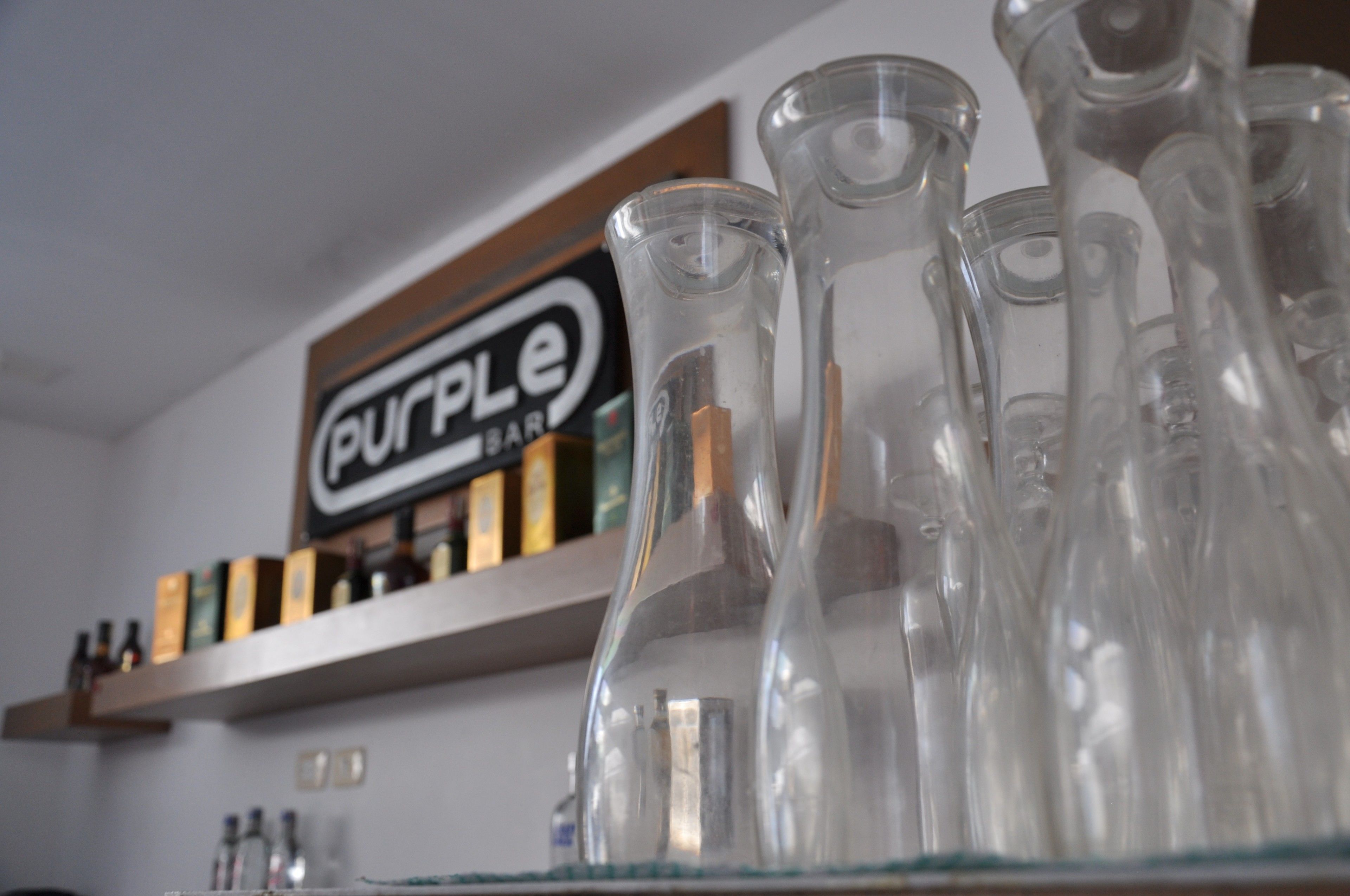 Un coin bar avec une enseigne indiquant « Purple Bar » et plusieurs bouteilles de verre vides sur une étagère.