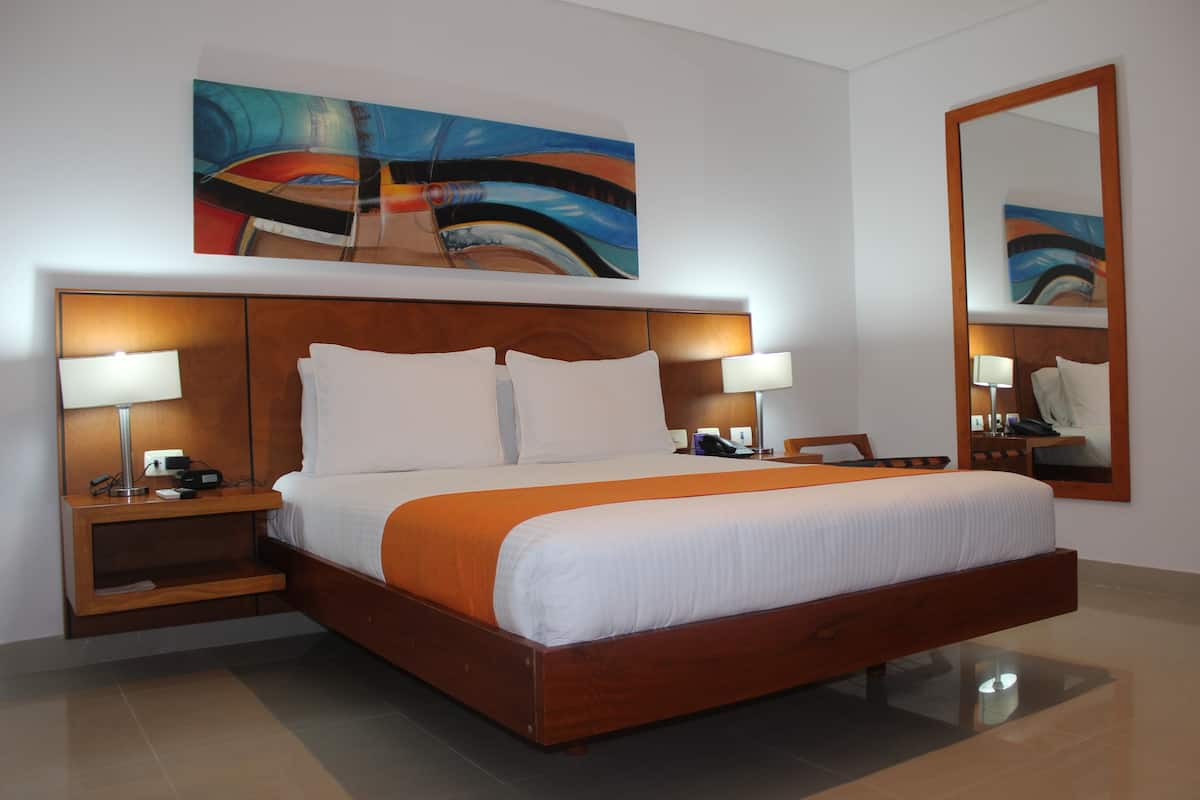 A hotel room with a wooden bed, two bedside tables with lamps, a large mirror, and a colorful abstract painting on the wall.