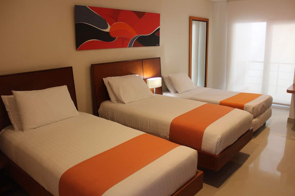 A hotel room with three beds, each with white bedding and orange accents. There is a large abstract painting on the wall above the beds, and a window providing natural light.