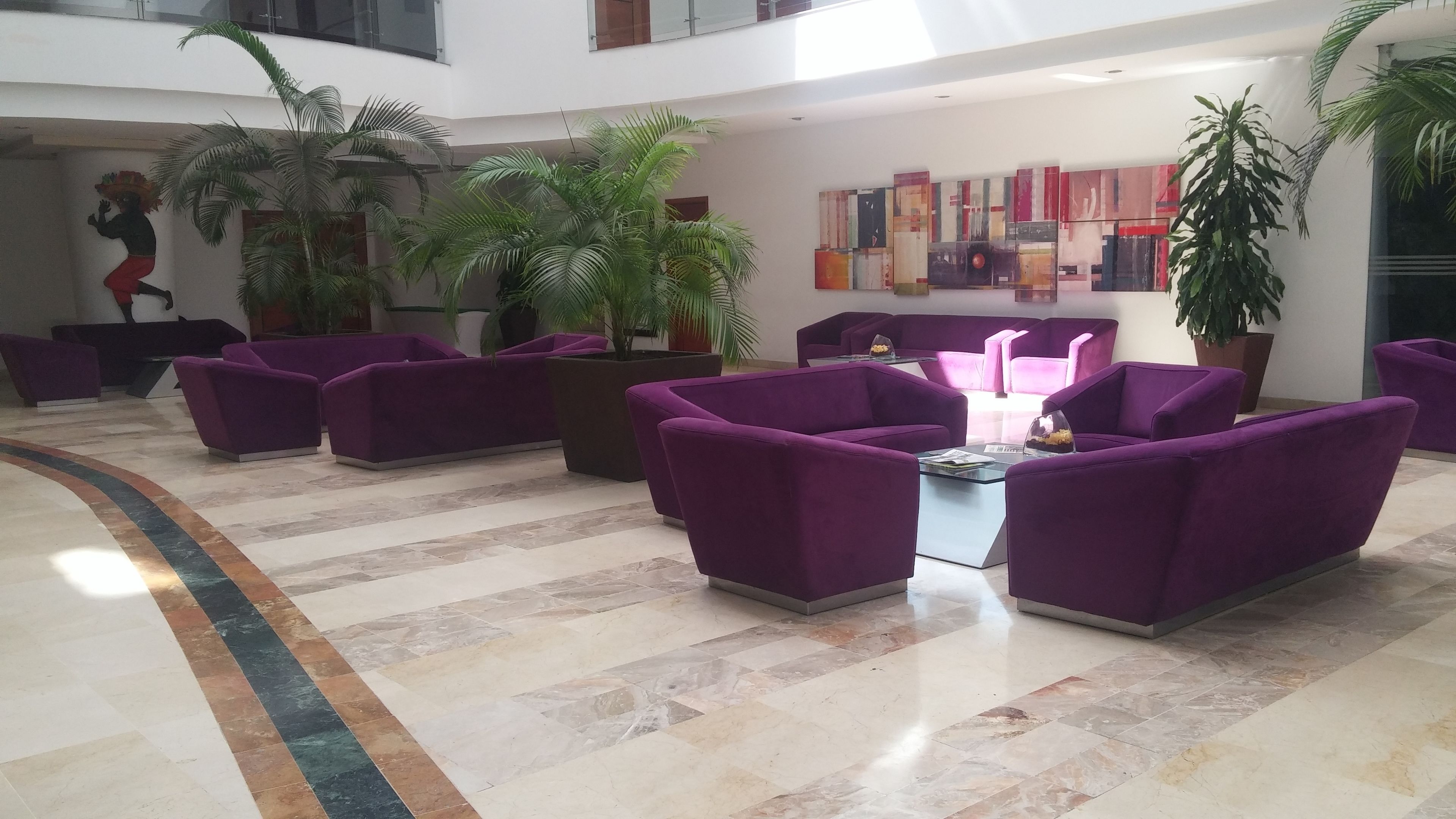 Un vestíbulo con asientos morados, piso de baldosas y plantas en macetas.