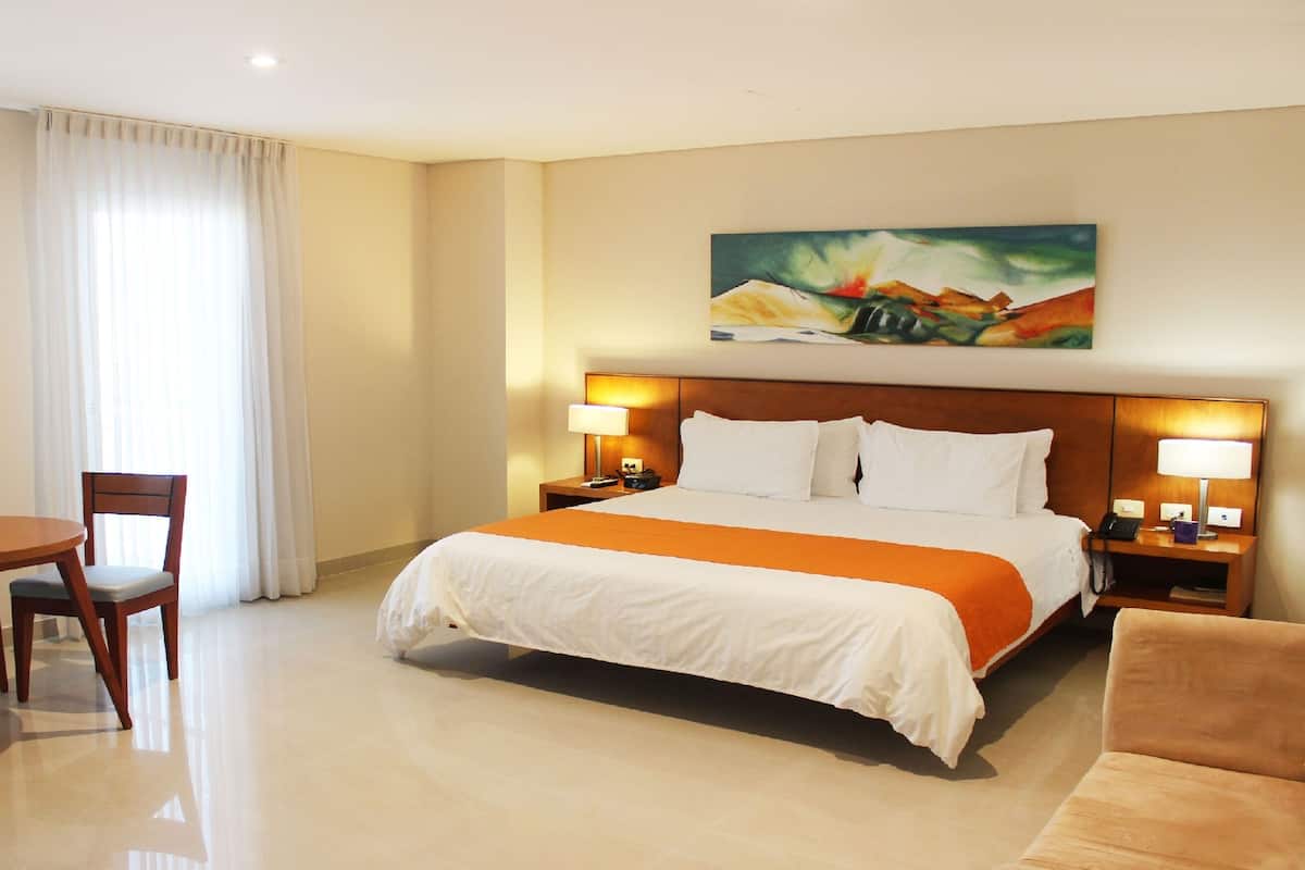 A hotel room with a large bed, two bedside tables with lamps, a desk with a chair, and a painting on the wall.