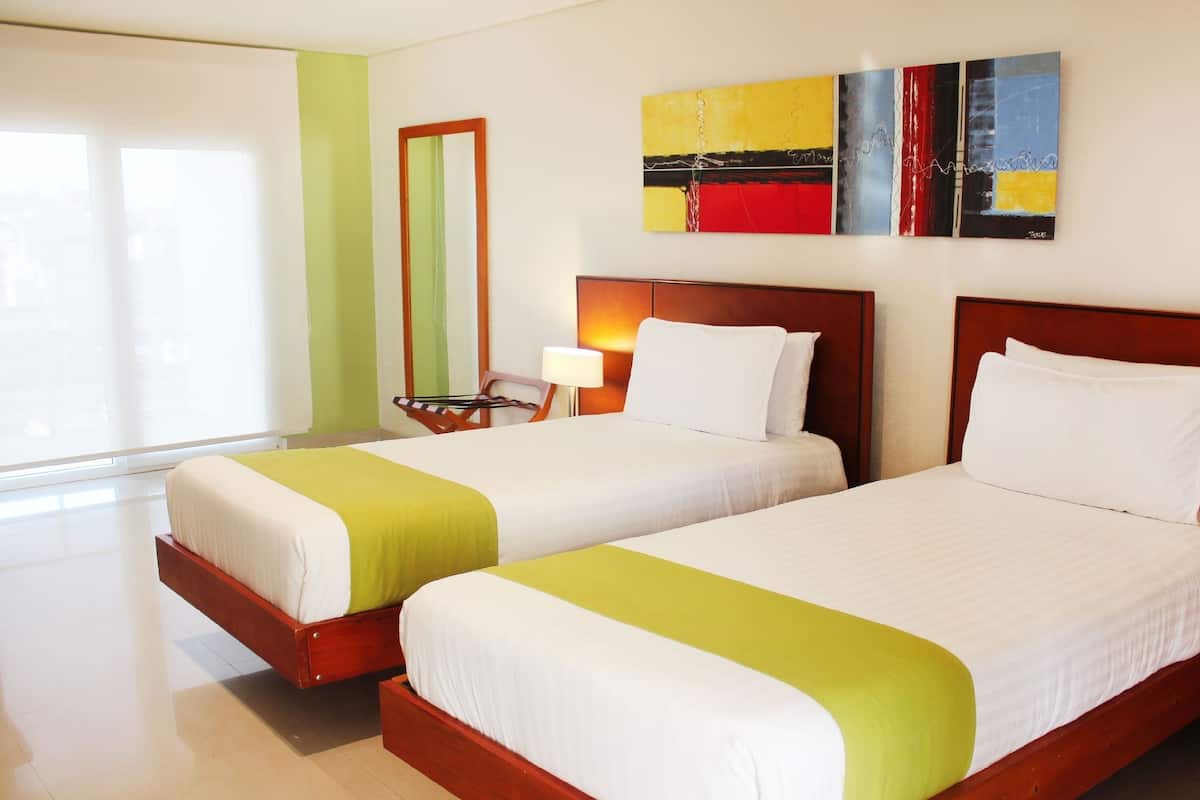 A hotel room with two beds, a mirror, a painting, and a window with blinds.