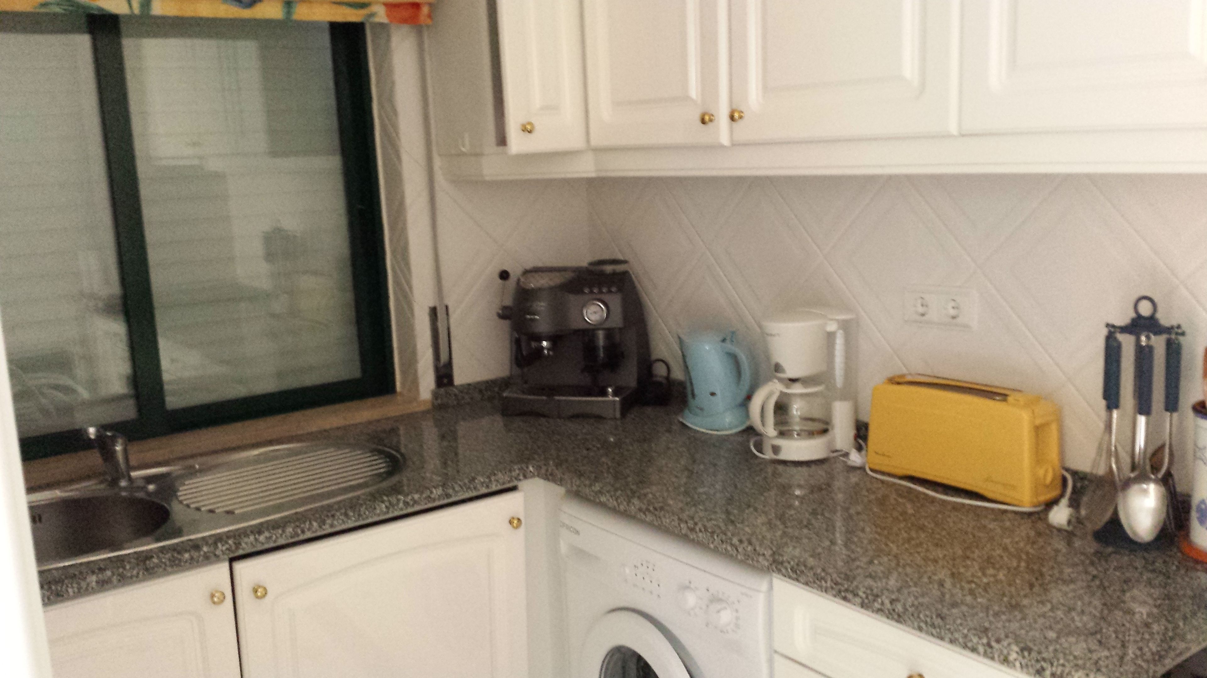 Une cuisine compacte équipée d’un lave-linge, d’une machine à café, d’un grille-pain et d’un évier.
