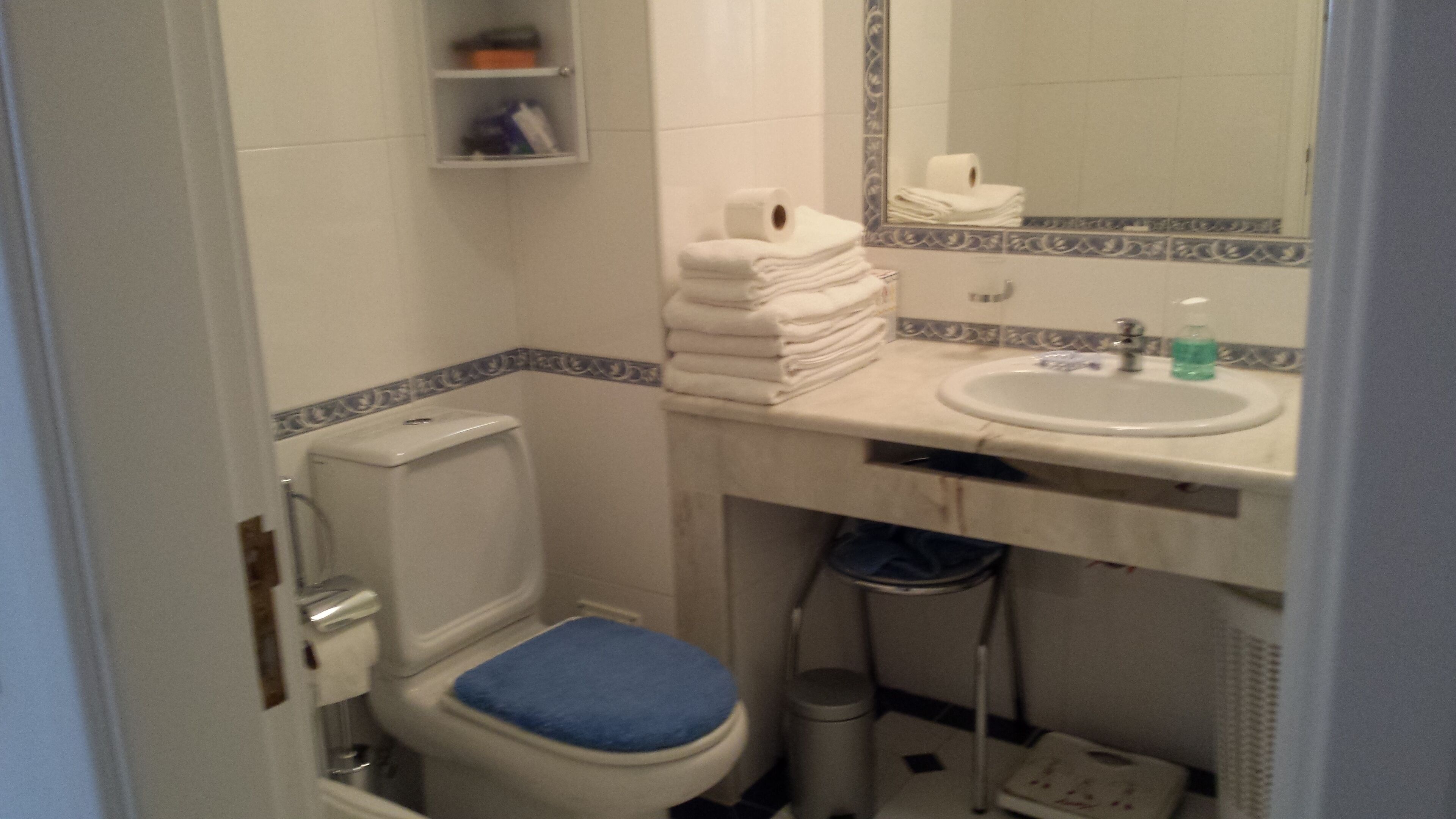 A small bathroom with a toilet, sink, and a mirror. There is a stack of white towels on the sink counter.