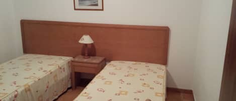 A small room with two single beds, a nightstand with a lamp, and a framed picture on the wall.