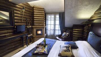 A log cabin-style room with a fireplace, a bed with a tray of wine glasses, and a television on a wooden table.