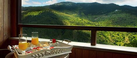 A balcony with a table set for breakfast, overlooking a mountainous landscape.