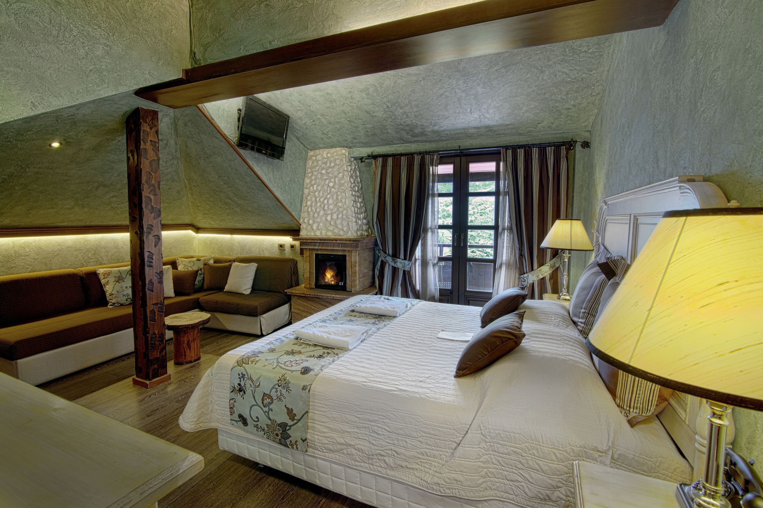 Un dormitorio con una cama grande, un sofá, una chimenea y una ventana con cortinas.