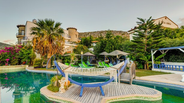 A pool area with a hammock, lounge chairs, and a view of a building with a sign. - Villa Asina (Datça)