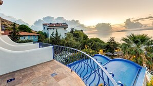 A pool area with a blue pool, a white building, and a view of the sea. - Villa Asina (Datça)