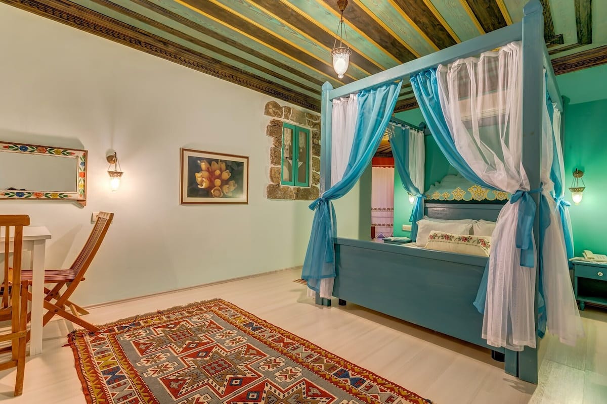 A bedroom with a four-poster bed, a patterned rug, and a wooden chair.