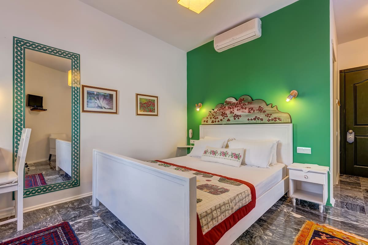 A bedroom with a green accent wall, a white bed with a floral headboard, a bedside table, and a nightstand.