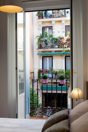 A hotel room with a balcony overlooking a building with multiple balconies adorned with potted plants and flowers. - THC Latina Hostel (Madrid)