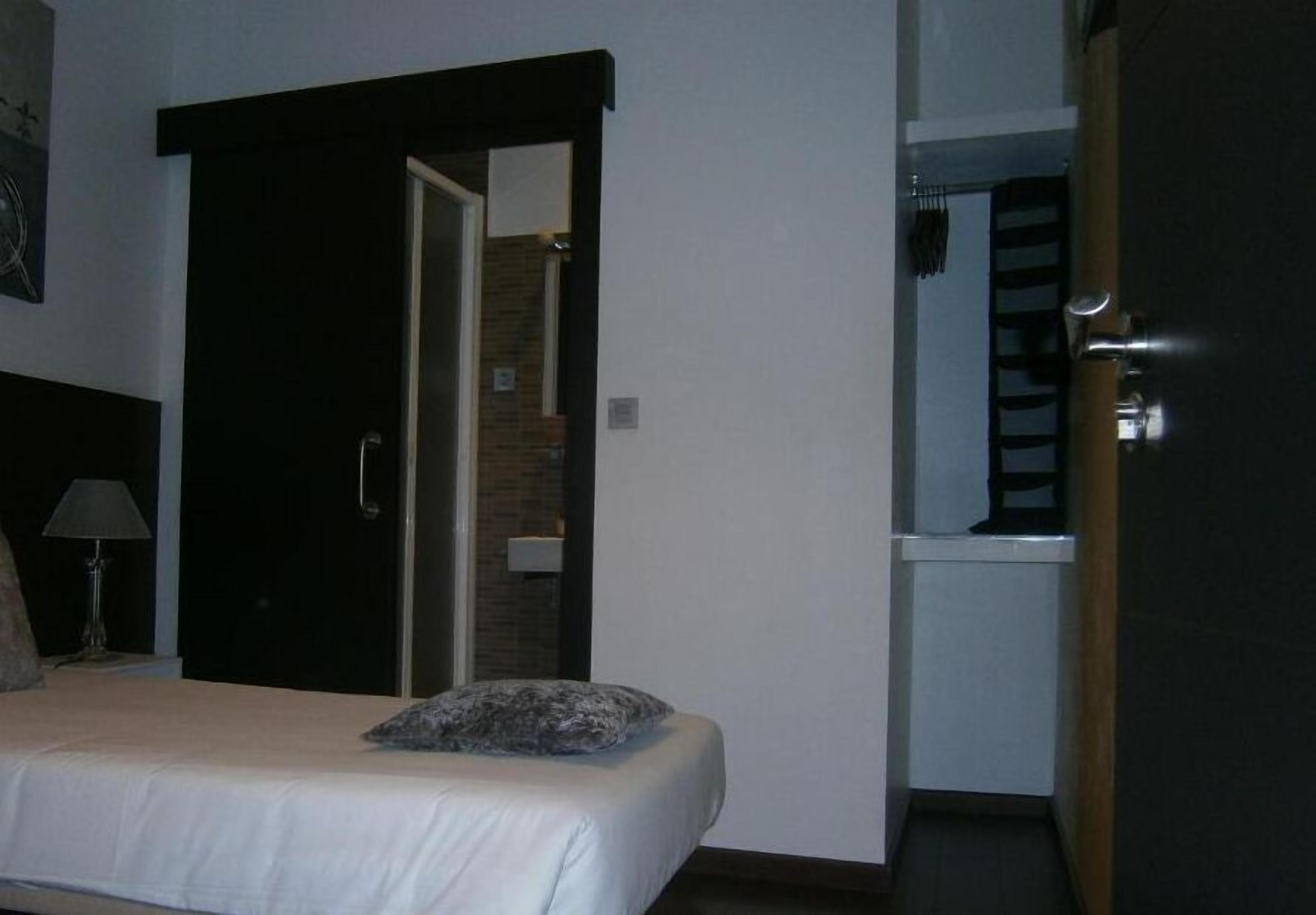 A hotel room with a bed, a nightstand with a lamp, a wardrobe, and a door leading to a bathroom.