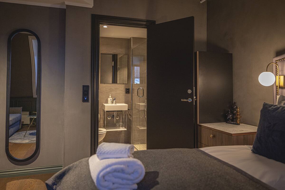 Habitación de hotel con cama, baño, espejo y mesita de noche con lámpara.