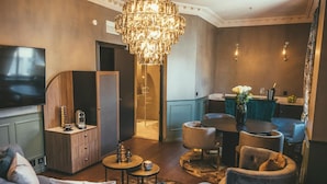 A modern living room with a large TV, a chandelier, and a dining area with a table and chairs.