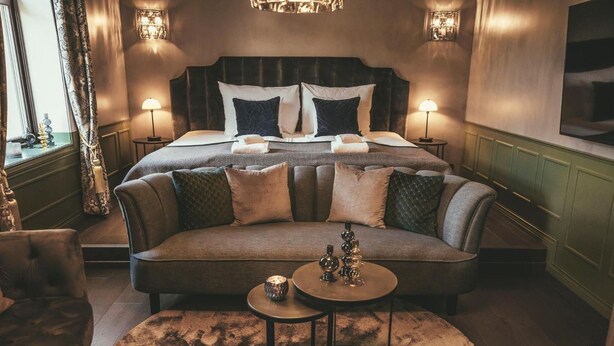 A luxurious bedroom with a large bed, a sofa, and a small table with decorative items.