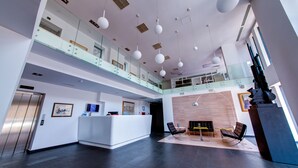 A modern lobby with a reception desk, seating area, and a glass railing overlooking the lower level. - Sarroglia (Bucharest)