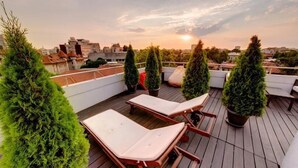 A rooftop terrace with two lounge chairs, potted trees, and a view of the cityscape during sunset. - Sarroglia (Bucharest)