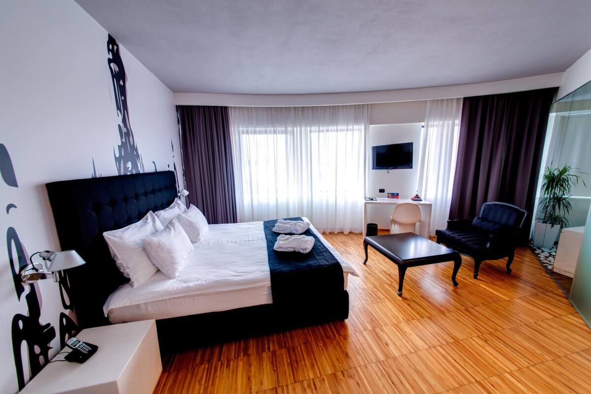 A hotel room with a large bed, a desk, a chair, a TV, and a plant.