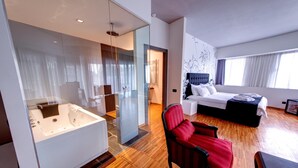 A modern hotel room with a large bathtub, a bed with a dark headboard, and a red armchair. - Sarroglia (Bucharest)