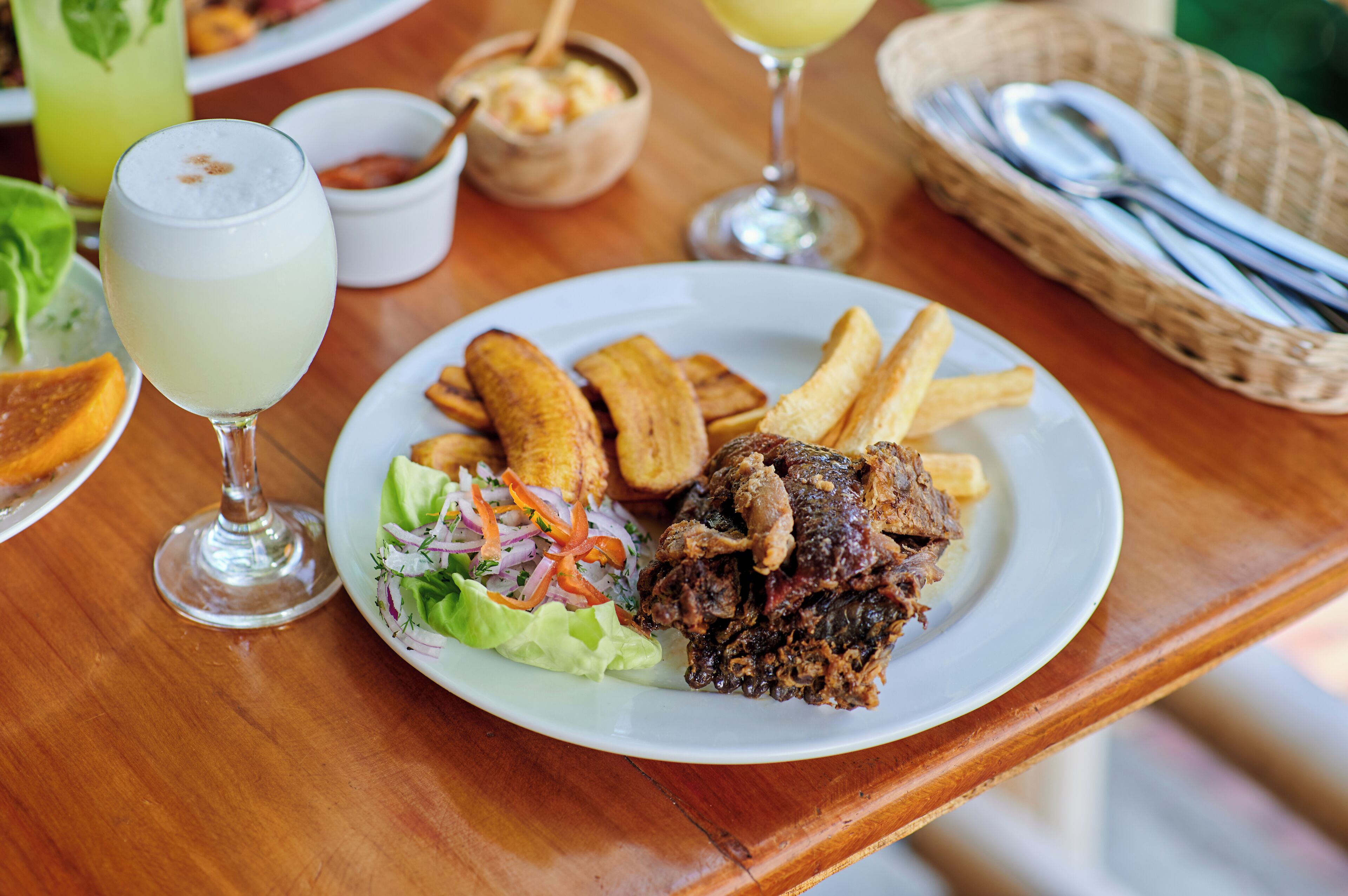 Una mesa de comedor con un plato de comida, un vaso de bebida y una cesta de cubiertos.