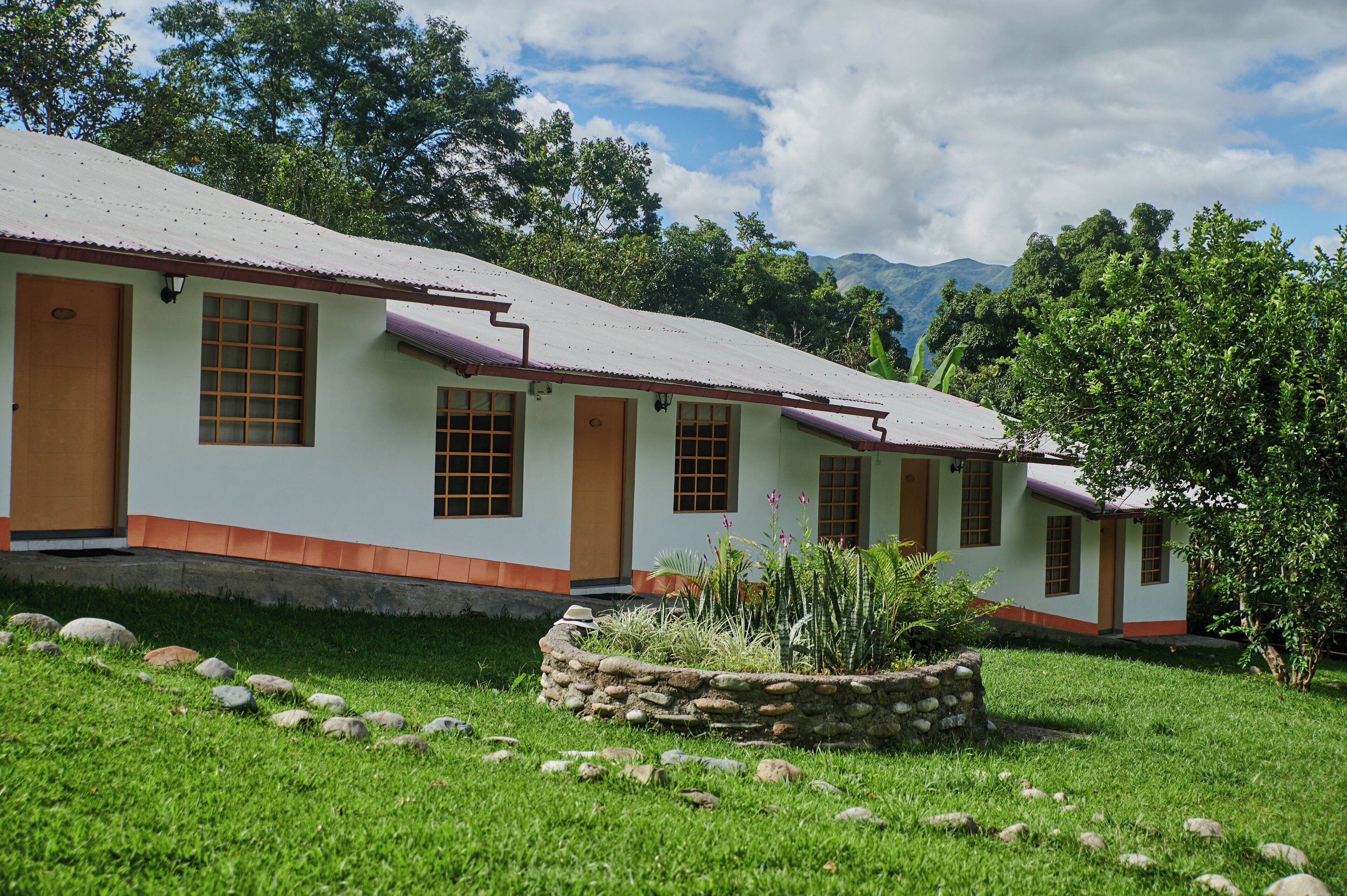 A row of white buildings with orange trim and wooden doors, surrounded by a well-maintained grassy area with rocks and plants.