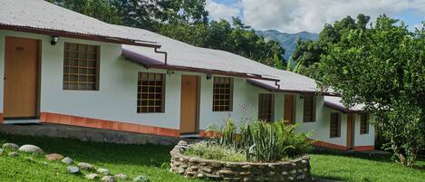 A row of white buildings with orange trim and wooden doors, surrounded by a well-maintained grassy area with rocks and plants.