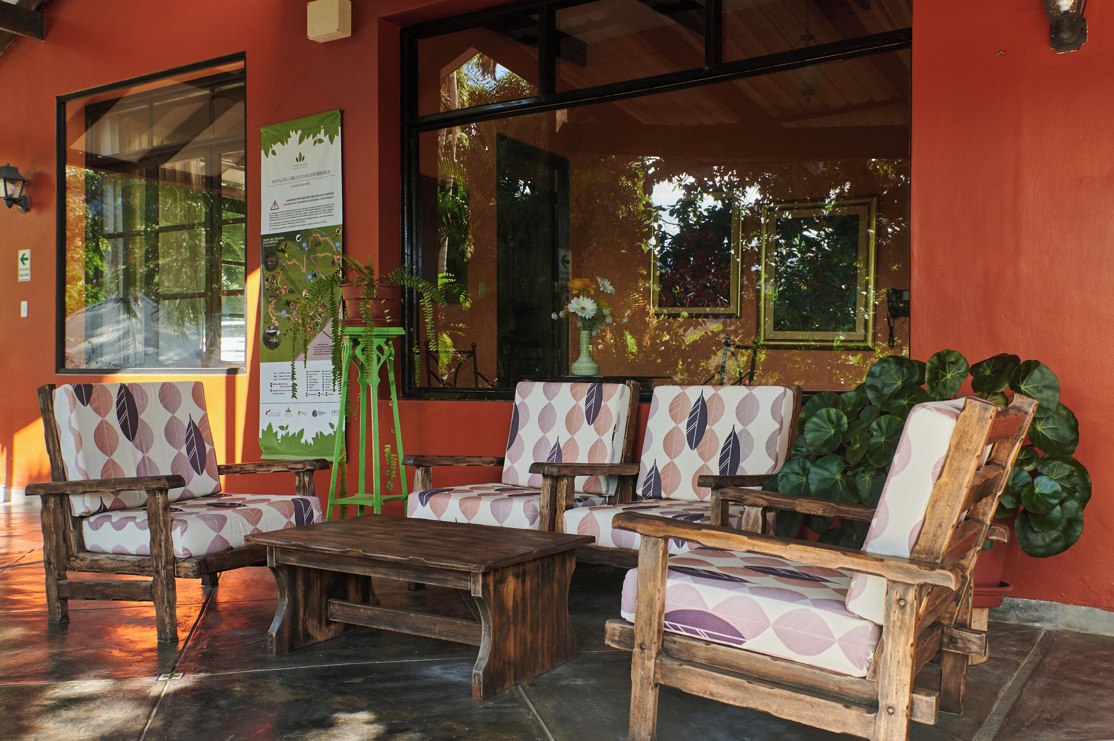 A seating area with wooden furniture and a table, large windows, and a potted plant.