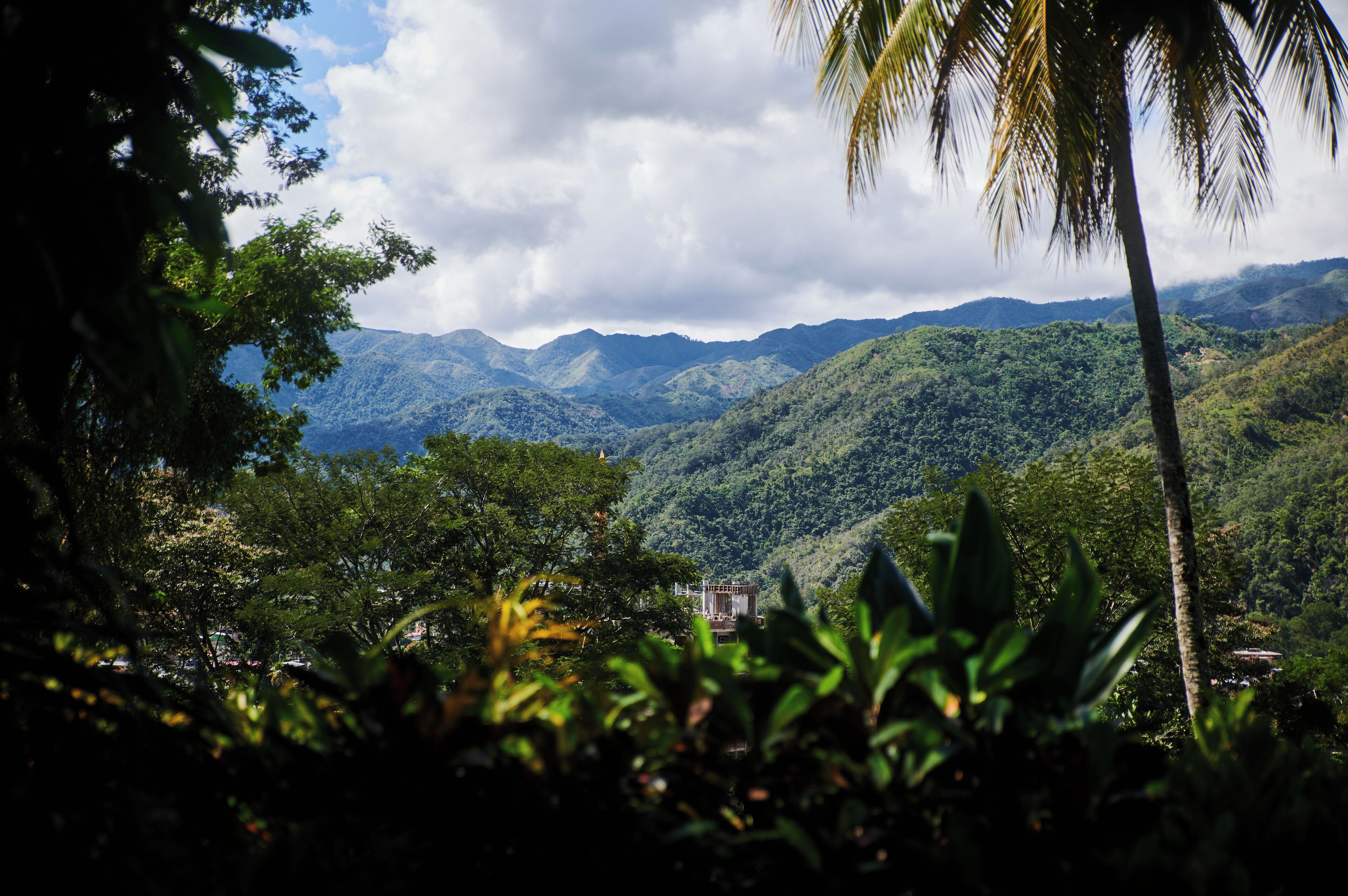 A lush, mountainous landscape with dense greenery and a few buildings in the distance.