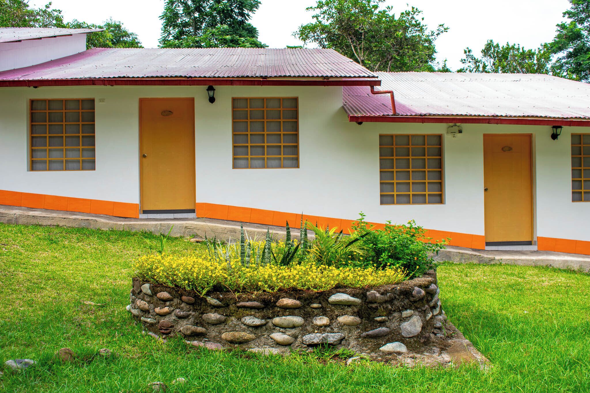 Un edificio con techo rojo, paredes blancas y detalles en color naranja. Tiene varias puertas y ventanas con marcos de madera.