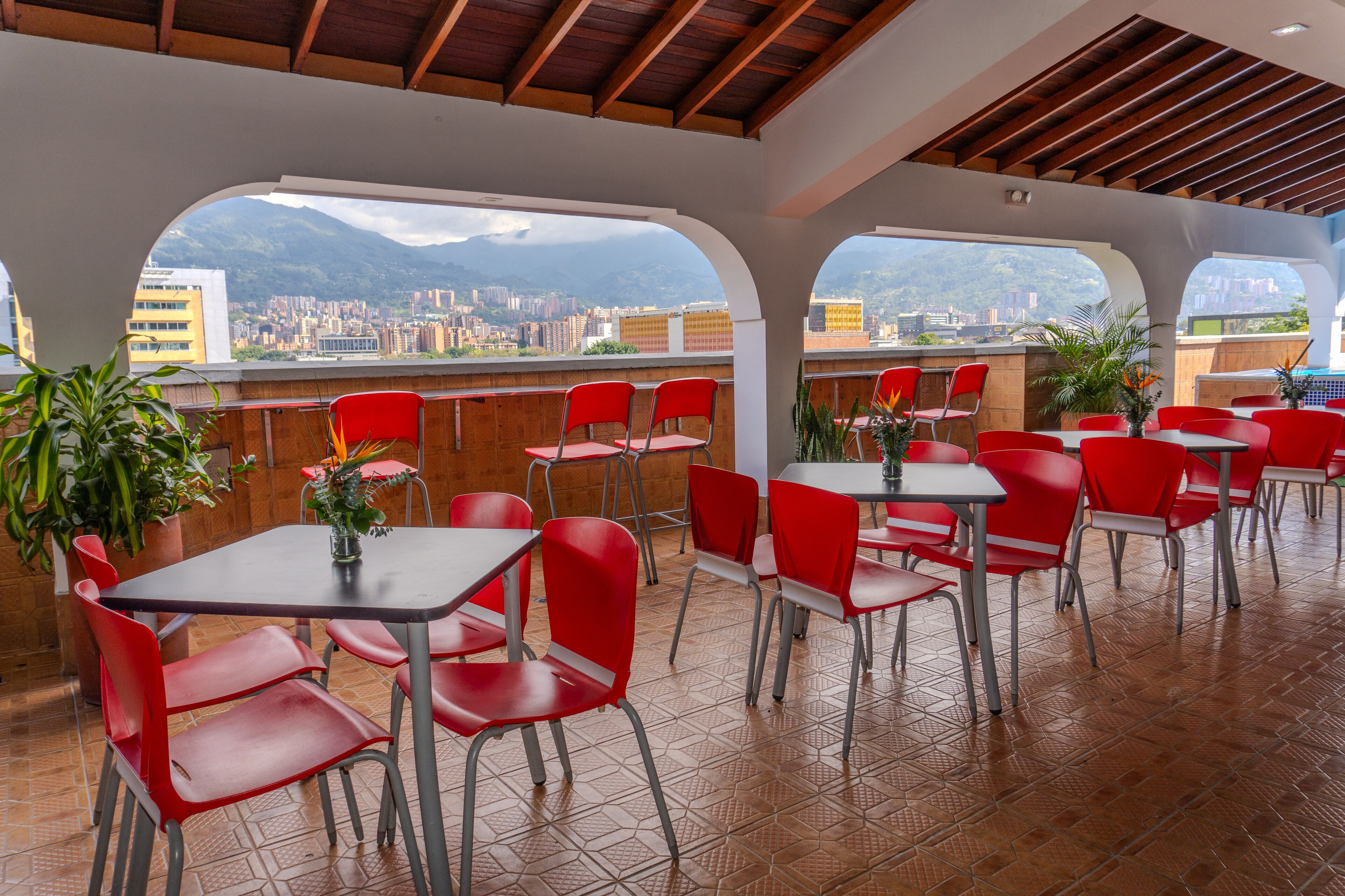 Un restaurant avec des chaises et des tables rouges, de grandes fenêtres donnant sur la ville et un sol carrelé.