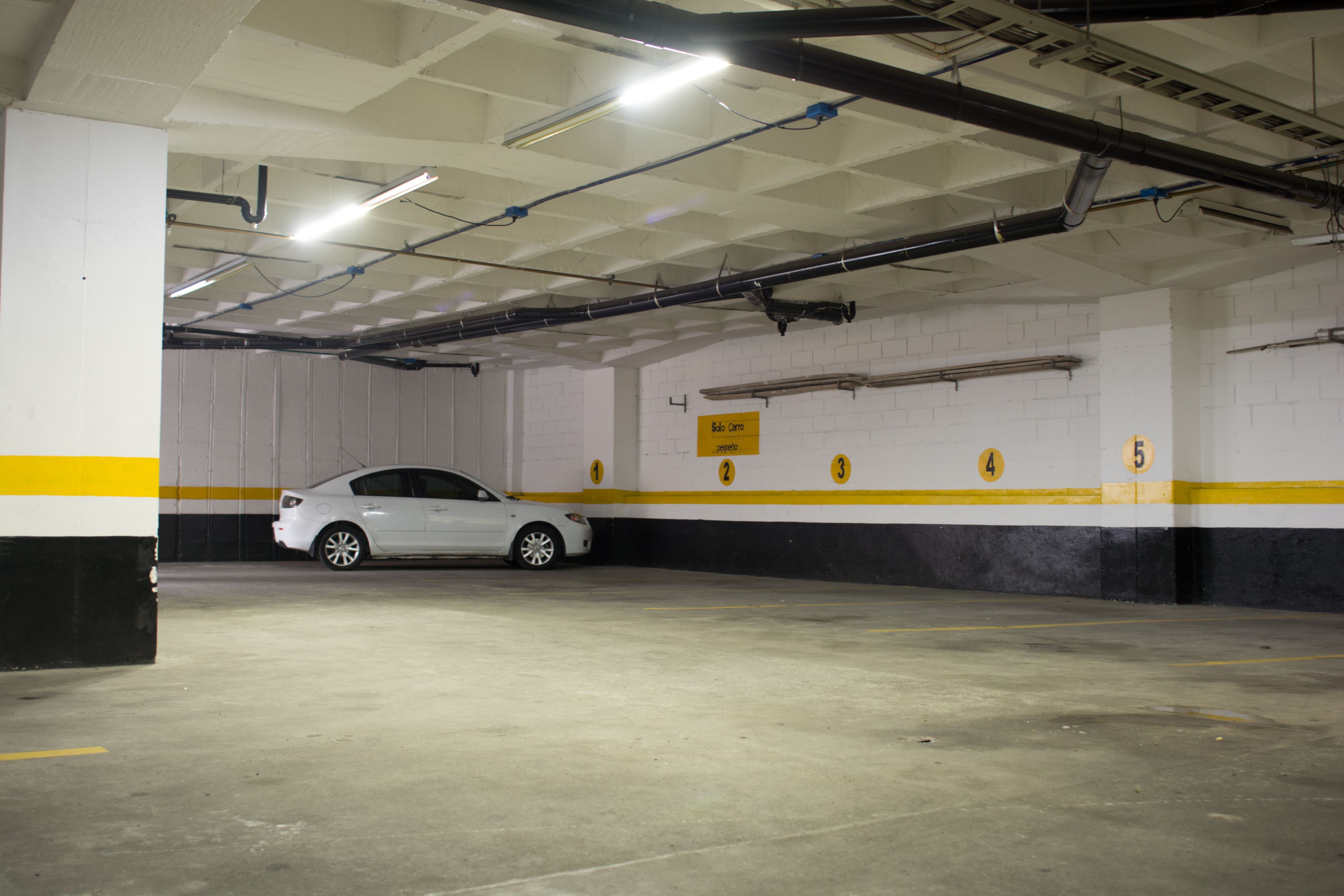 A parking garage with a white car parked in a spot marked with numbers 1 to 5.