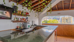 A kitchen with a large island, hanging plants, and a city view through a window. - Hotel Alcaravan Medellín (Itagüí)