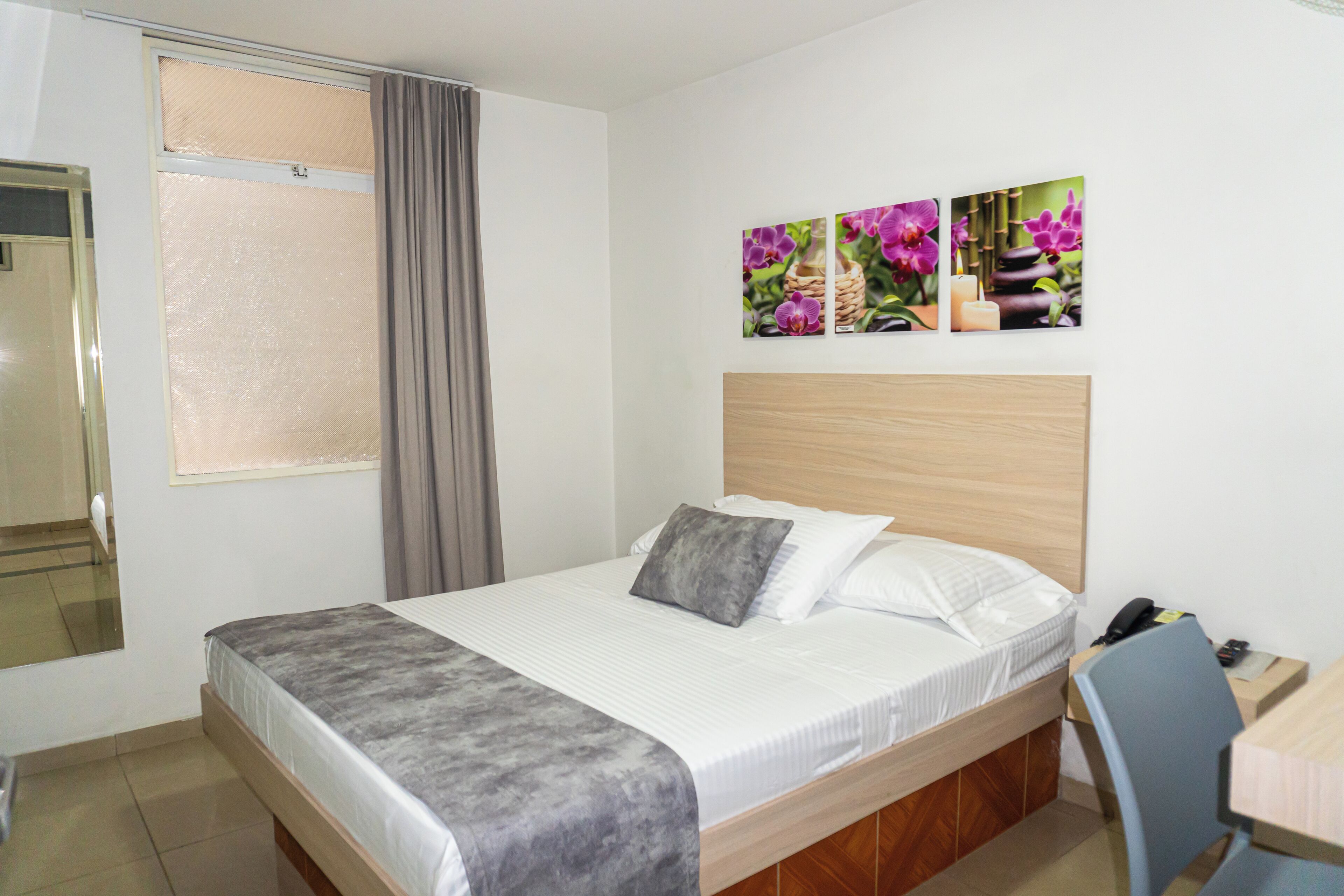 Ein Hotelzimmer mit Bett, Schreibtisch, Stuhl, Spiegel und einem Fenster mit Vorhängen.