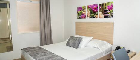 Ein Hotelzimmer mit Bett, Schreibtisch, Stuhl, Spiegel und einem Fenster mit Vorhängen.