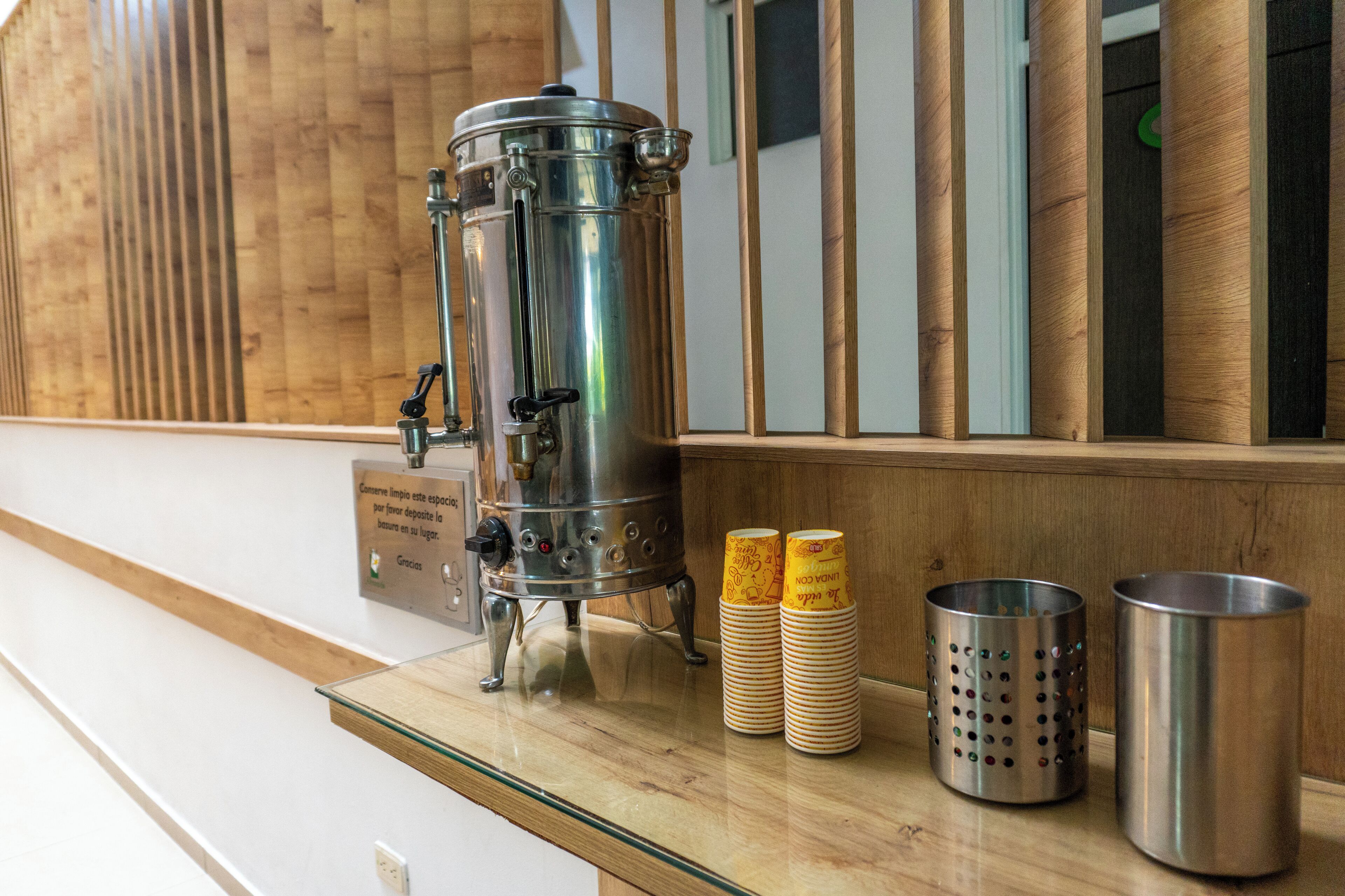 A stainless steel coffee machine on a wooden counter with stacked disposable cups and a metal container.